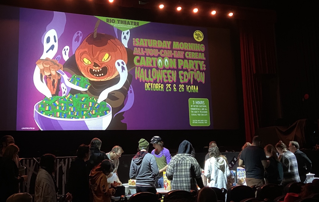 Movie screen showing the morning cartoons banner and people getting their cereal at front of house cereal table.