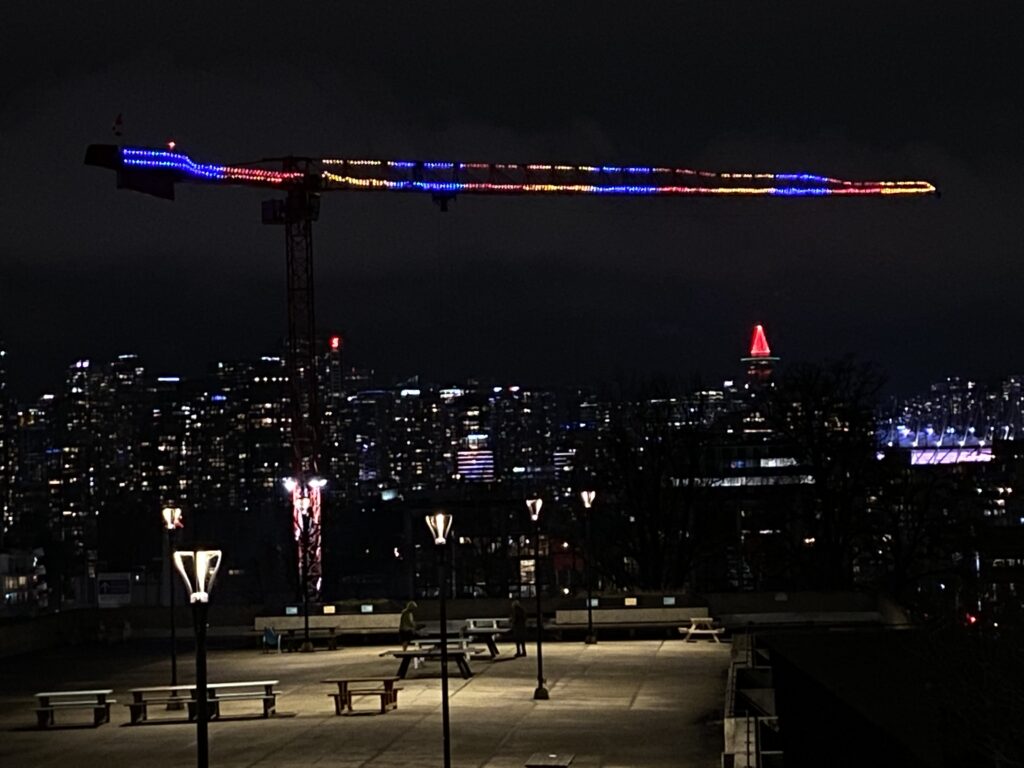 Christmas lights on a crane with Vancouver in the background and a plaza in the foreground.